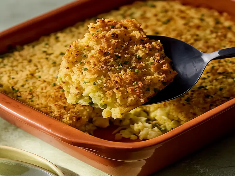 Golden-baked shredded zucchini casserole topped with melted cheese and crispy breadcrumbs, served in a white baking dish.