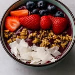 Thick acai smoothie bowl topped with banana slices, blueberries, pomegranate and coconut flakes.