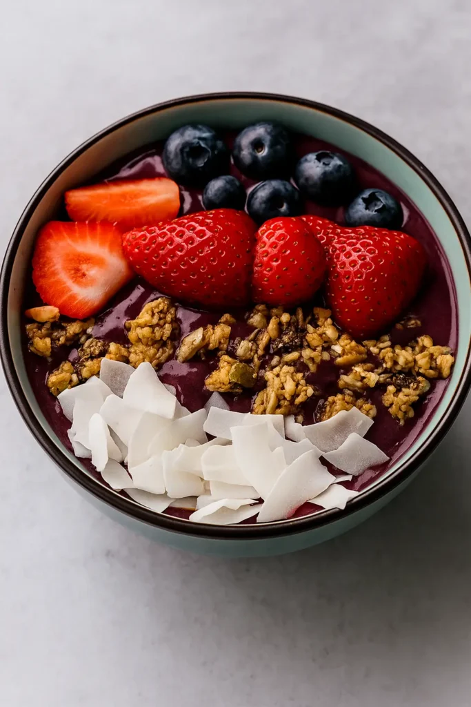 Thick acai smoothie bowl topped with banana slices, blueberries, pomegranate and coconut flakes.