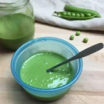 Smooth green pea puree in a small bowl with a baby spoon.