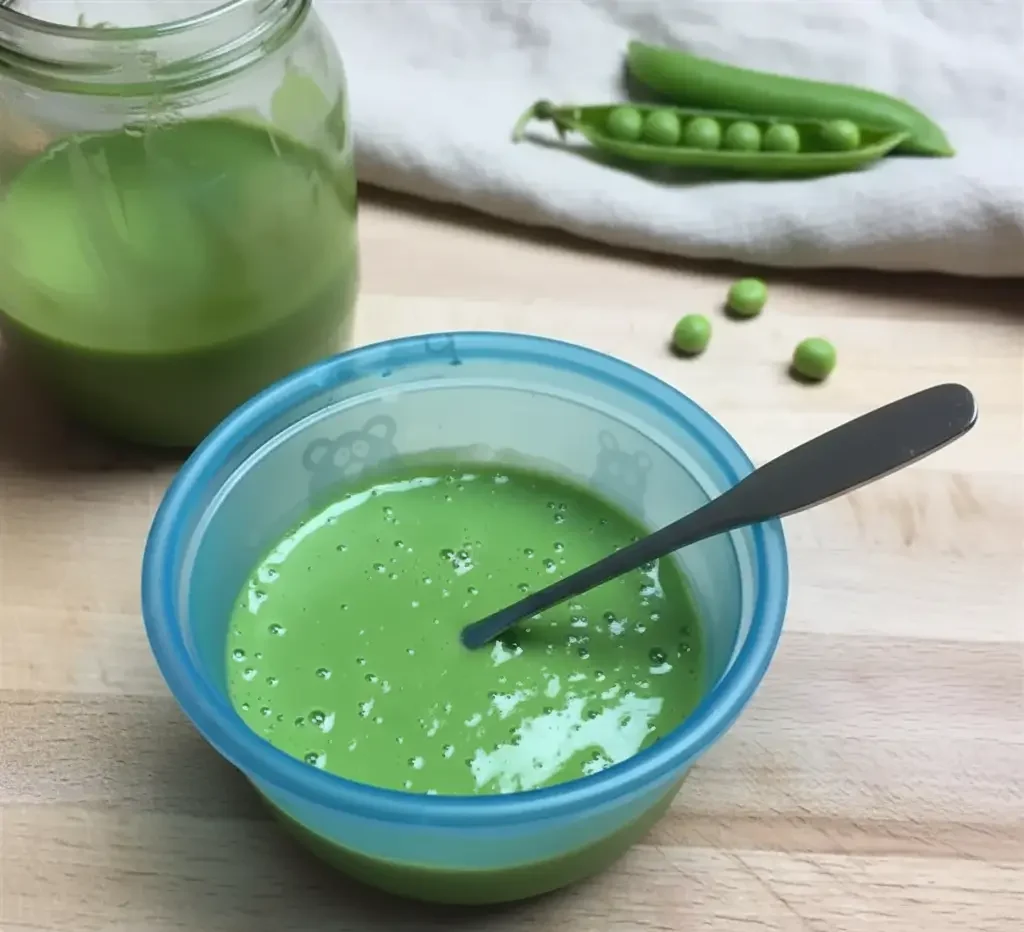 Smooth green pea puree in a small bowl with a baby spoon.