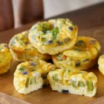 Twelve golden mini muffin pan frittatas garnished with chives on a cooling rack.