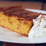 Pumpkin soufflé casserole in a square baking dish dusted with cinnamon.