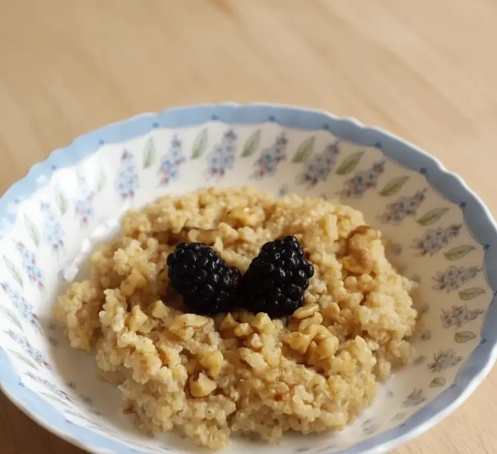 Bowl of warm quinoa porridge topped with cinnamon and sliced fruit.