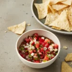 Fresh homemade salsa in a bowl with cilantro and lime wedge on the side.
