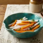 Bright pink and white pickled daikon radish and carrot matchsticks in a glass jar with cilantro and chili.