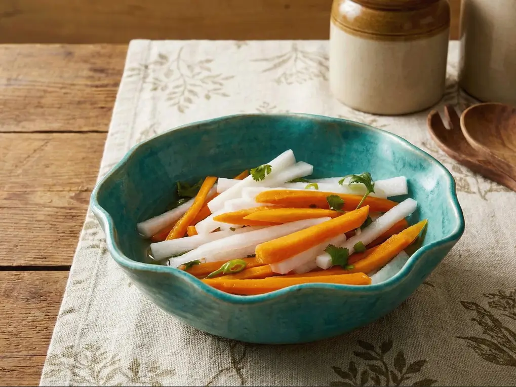 Bright pink and white pickled daikon radish and carrot matchsticks in a glass jar with cilantro and chili.